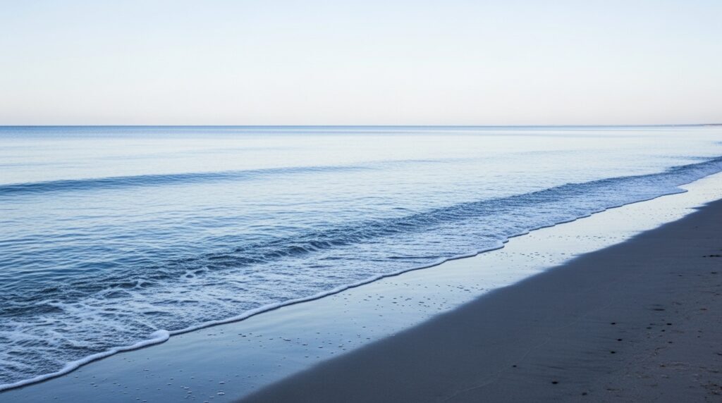 Blass-blaue Küstenlandschaft mit zurückweichendem Wasser und sauberem Sand – symbolisiert Rückkehr und Erneuerung